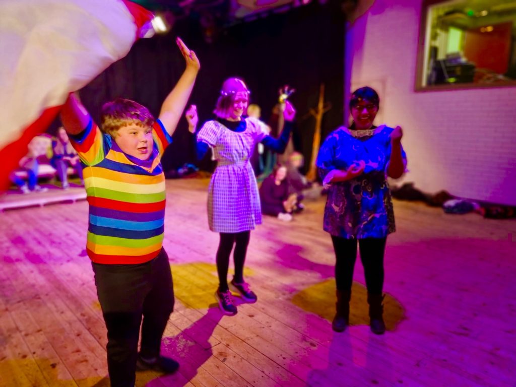 Three young people, members of the New Vic Borderlines Young People's Theatre Company, enjoy themselves dancing and waving a flag.