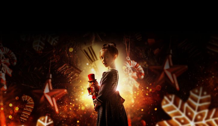 A girl in period dress holds a nutcracker, surrounded by snowflakes.