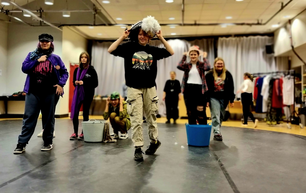 New Vic Borderlines' Young People's Theatre Company rehearse for a show. In the foreground one of the members tries on a hat.