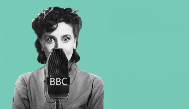 A woman in period dress behind a radio microphone