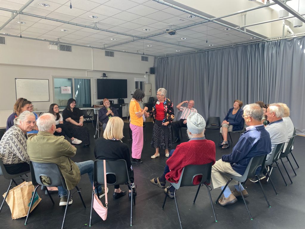 Told by an Idiot help the Dementia and Creativity Group brush up on their drama skills. The group sit in a circle around other participants performing in the middle. 