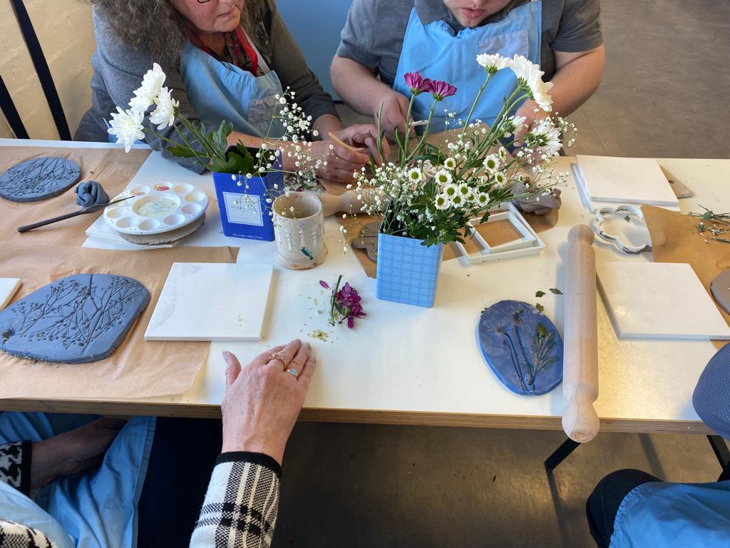 Participants of the workshop at World of Wedgwood press wildflowers into their clay tiles.
