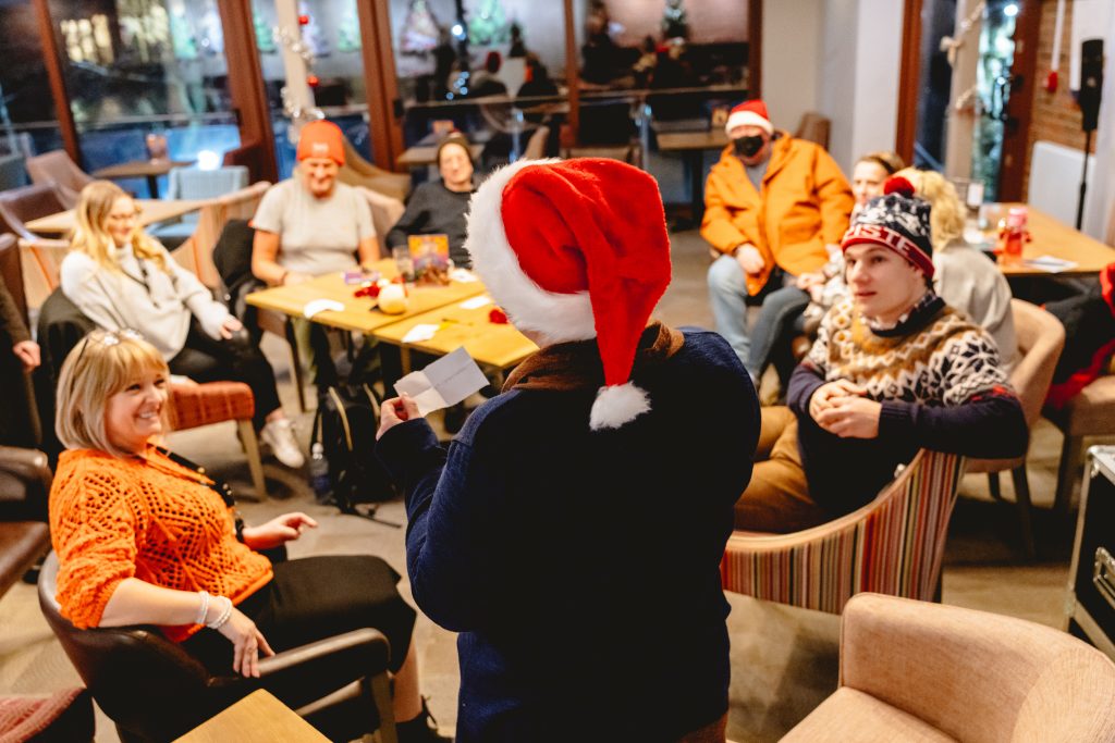 The group gathers around as a person wearing a santa hat reads a charade. Picture from Next Chapter Christmas quiz night in the New Vic bar. Credit: Andrew Billington