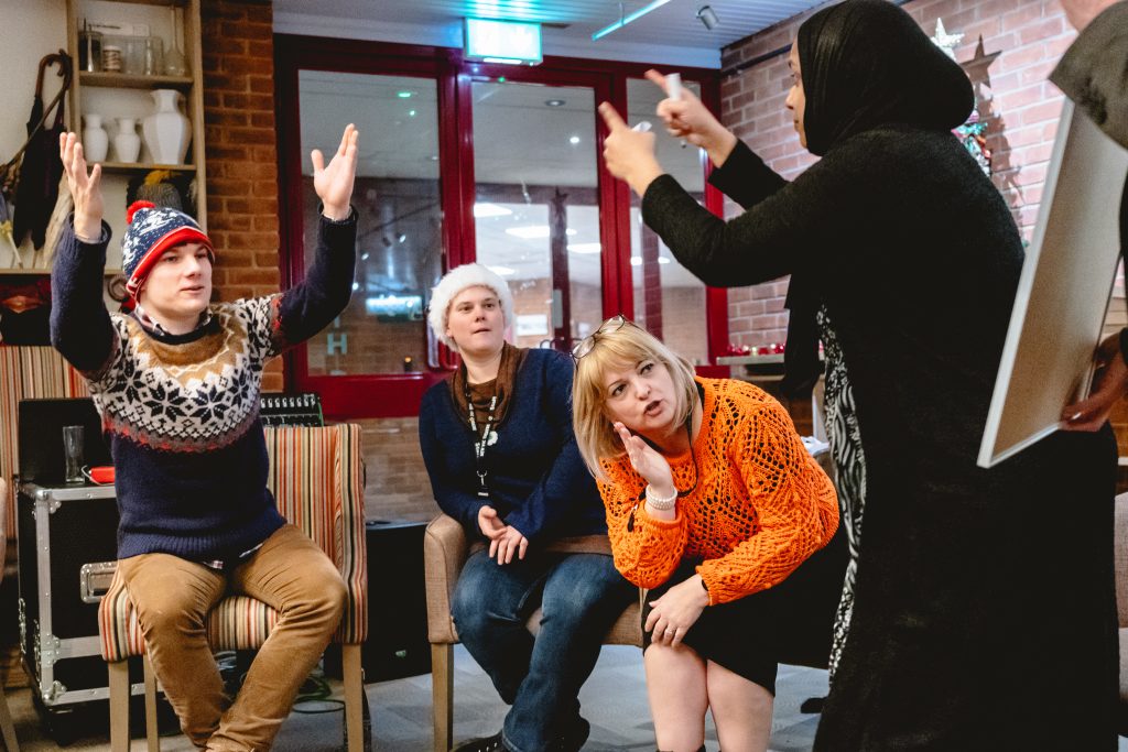 A woman in a hijab acts out a charade while others expressively guess what it could be. Picture from Next Chapter Christmas quiz night in the New Vic bar. Credit: Andrew Billington