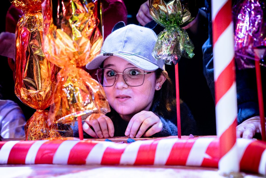 A girl with a mouse cap on perches her fingers on a ledge, surrounded by sweets. Picture from the Borderlines Young People's Theatre Company's version of The Nutcracker 2023. Credit: Andrew Billington