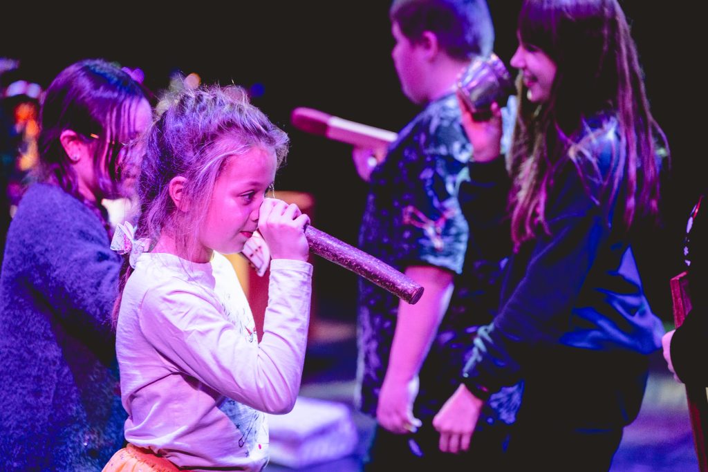 Performers use props to disguise themselves. One in the foreground puts a chunky twig over her nose. Young people dance in celebration. Picture from the Borderlines Young People's Theatre Company's version of The Nutcracker 2023. Credit: Andrew Billington