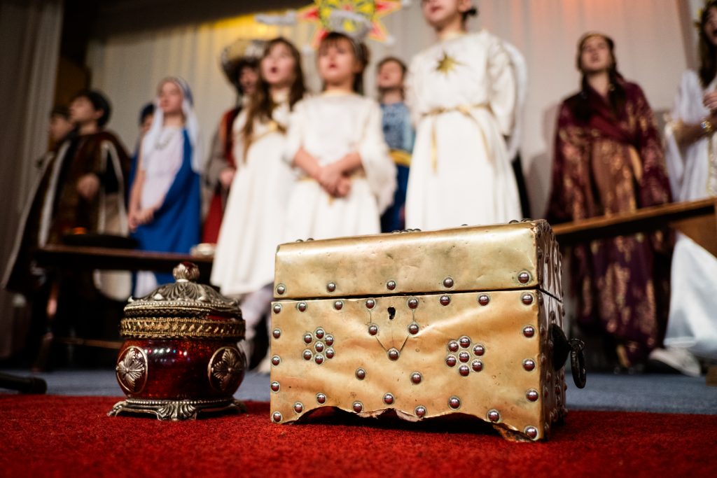 The nativity is performed in the background while the focus on the foreground is on the wise men's gifts. Picture from the Vertep at Newcastle Congregational Church, performed by Ukrainian families. Credit: Jenny Harper. 