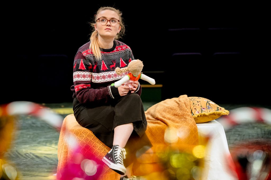 A girl in a Christmas jumper holds a doll and looks out into the distance. Picture from the Strathcross version of The Nutcracker 2023. Credit: Andrew Billington