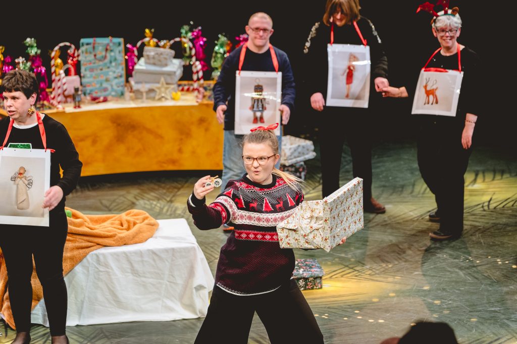 A girl unwraps a present. It's a small tank toy and she looks excited. Picture from the Strathcross version of The Nutcracker 2023. Credit: Andrew Billington