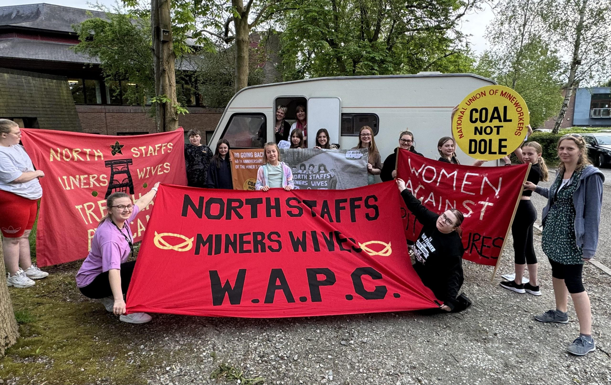 Members of New Vic Borderlines' Young People's Theatre Company with the 'Pit Camp Caravan', holding banners and signs with messages like 'North Staffs Miners Wives' and 'Coal not Dole'